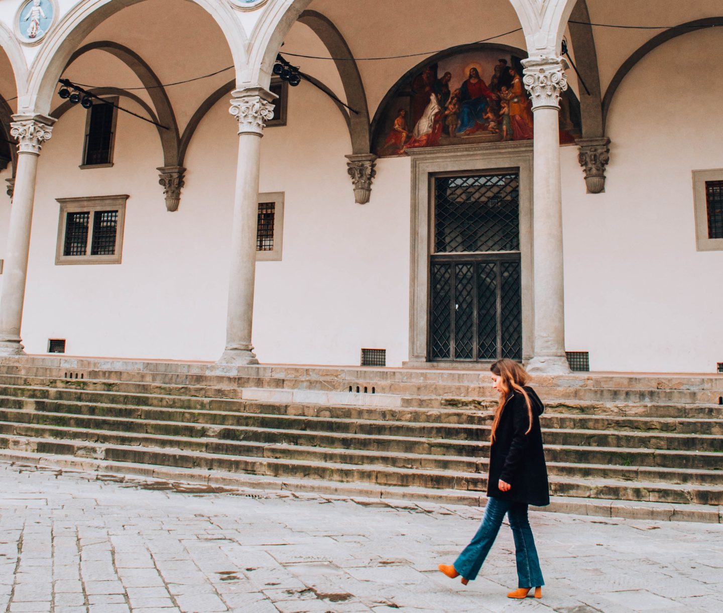 cosa mi piace fare a Firenze: ragazza di profilo con cappotto nero che cammina sotto arcate rinascimentali