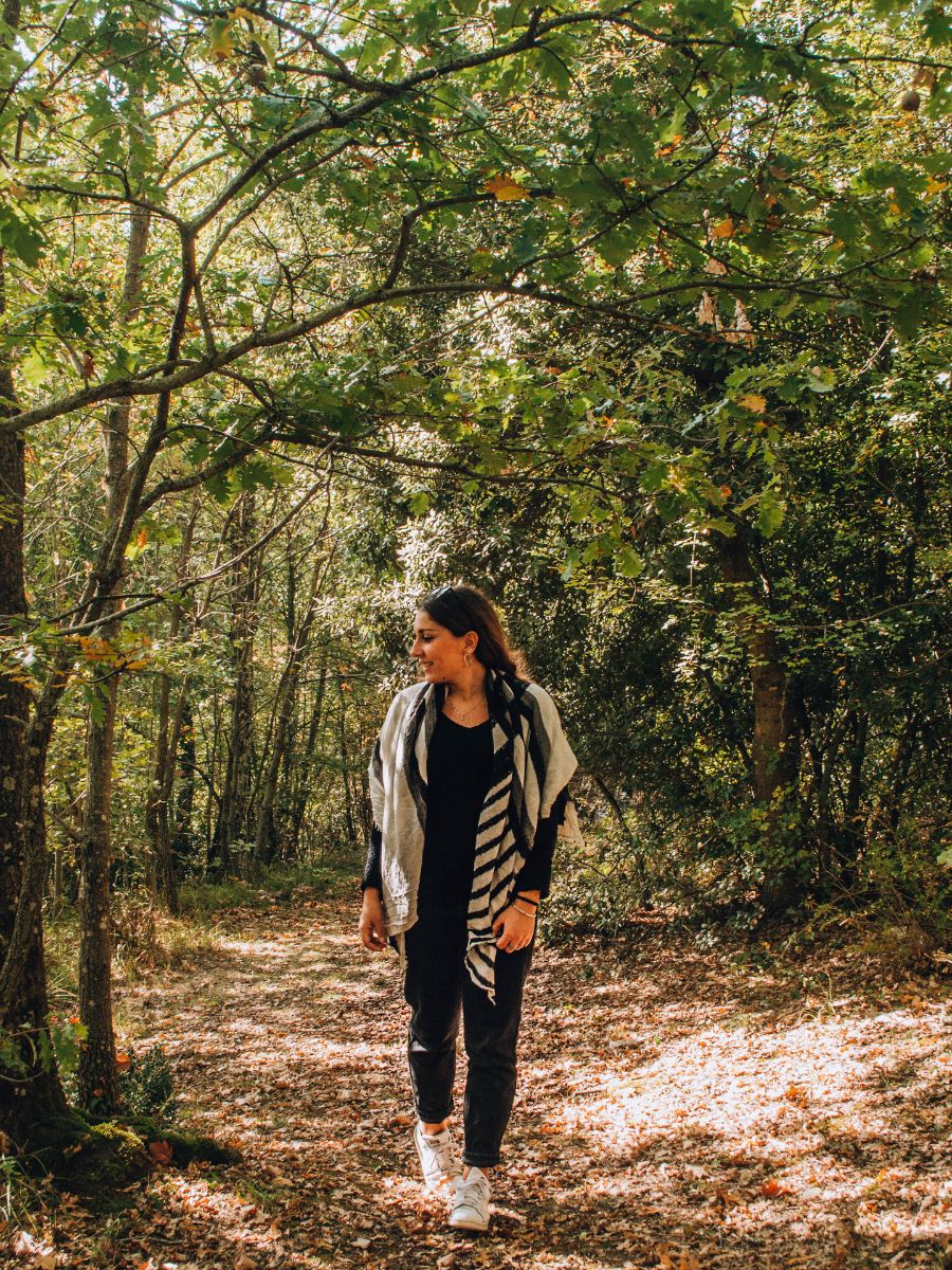 Ragazza con scialle a righe che passeggia tra le foglie cadute nel Bosco dei Cappuccini a Montepulciano.