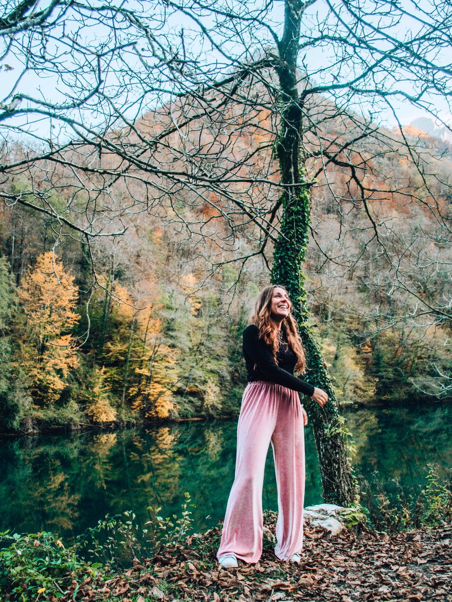 Ragazza in pantaloni rosa sorridente in riva al lago di Isola Santa in Garfagnana circondato dagli alberi autunnali.