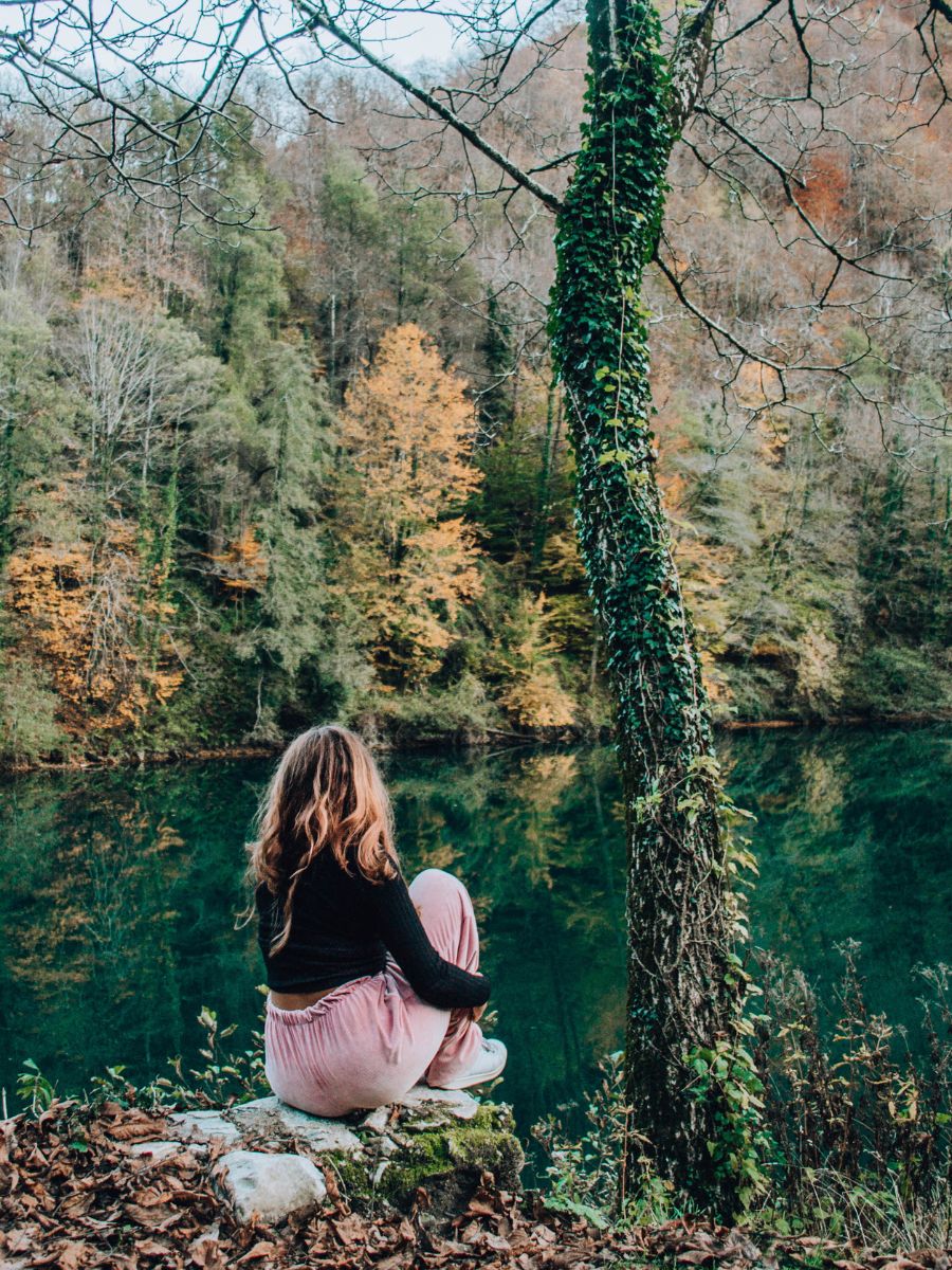 Ragazza seduta di schiena sul bordo del lago di Isola Santa mentre ammira i colori del foliage in Garfagnana.