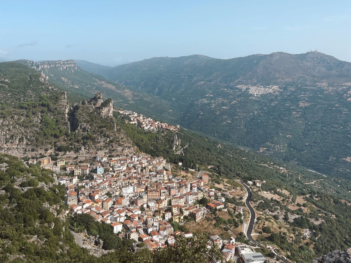 Suggestiva veduta aerea di Ulassai, cosa vedere per gli amanti dei panorami mozzafiato, con il borgo adagiato sul fianco della montagna e la vasta vallata verdeggiante che si estende all'orizzonte.